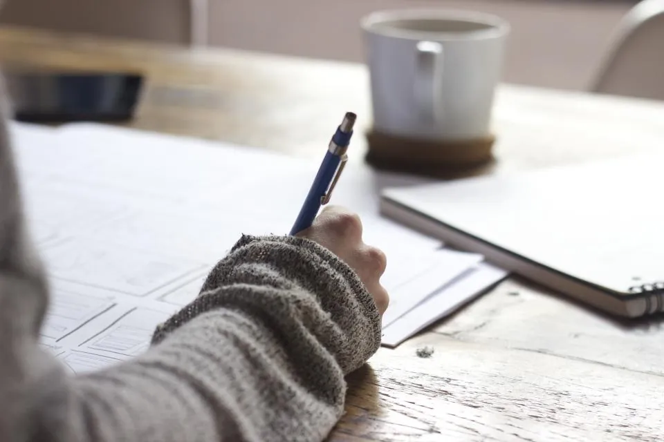 Hand sketching a plan on paper beside a coffee cup (stock photograph)